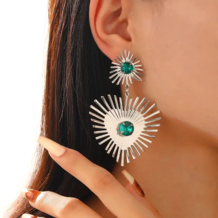 emerald sunburst statement earrings in silver with vivid green stones shown on ear, offering striking modern shine and sculpted spokes