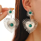 emerald sunburst statement earrings in silver with radiant spokes and green crystal center, displayed on ear for bold modern style
