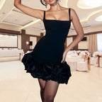 cocktail dress in classic black with square neckline and sculptural ruffle bottom, photographed in upscale event venue with elegant lighting