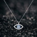 Evil eye protection necklace on textured black surface showcasing silver pendant with blue center stones.