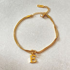 Gold bracelet with a 'E' charm on a light gray background