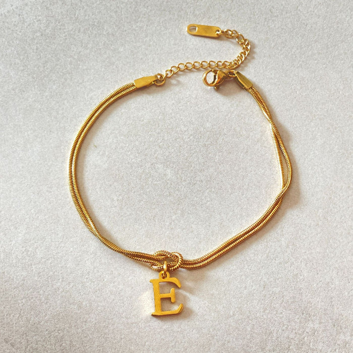 Gold bracelet with a 'E' charm on a light gray background
