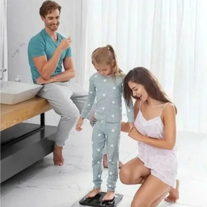 Family using smart body scale together in bathroom, mother helping child measure weight while father watches