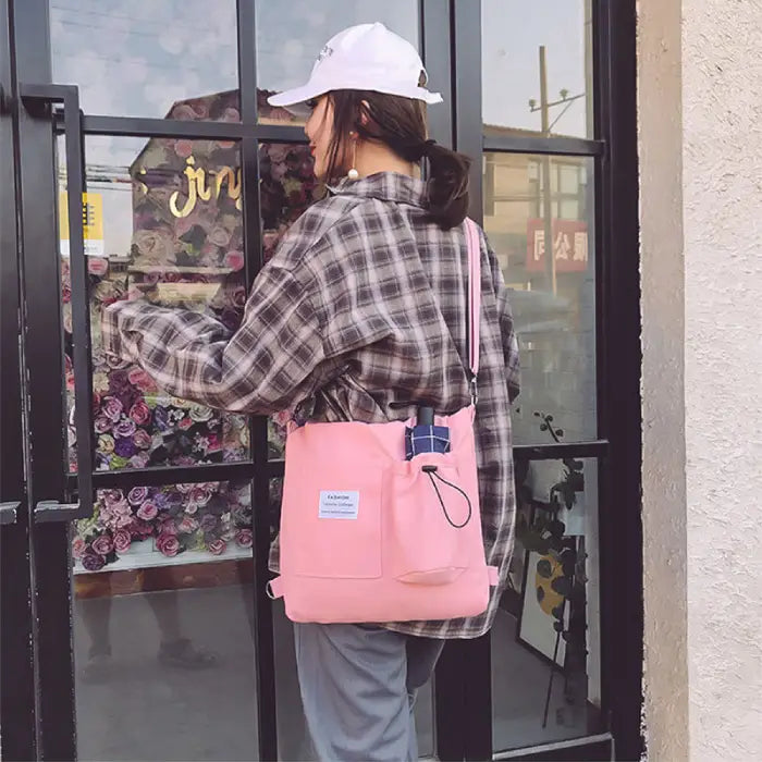 Pink canvas tote bag worn with plaid shirt and baseball cap near floral shop window