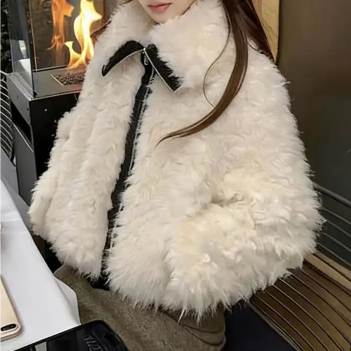 faux fur jacket, cropped ivory with black trim and high collar, plush winter layer shown on model by a fireplace inside.