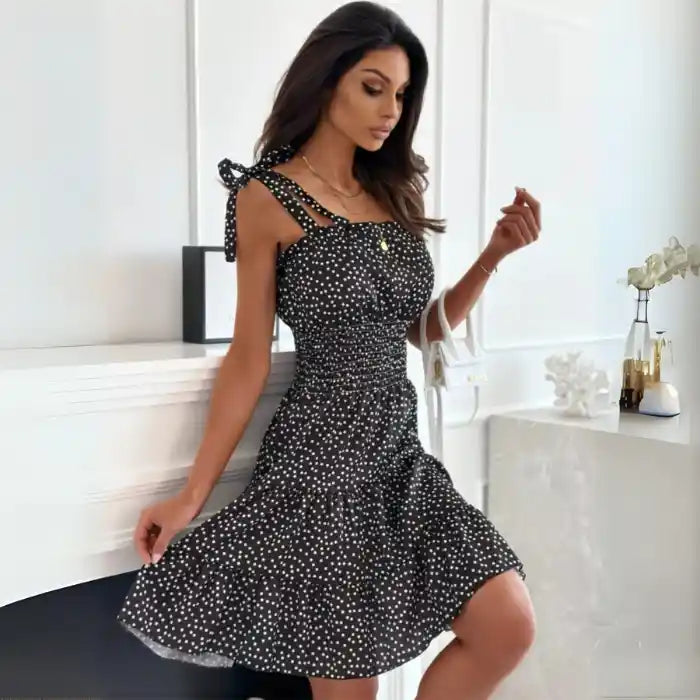 Feminine black dress with smocked top and flared hem styled with white handbag and heels