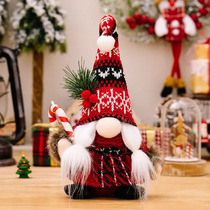 Christmas gnome with a red and black patterned hat, holding a candy cane, displayed with pine sprigs and holiday decorations