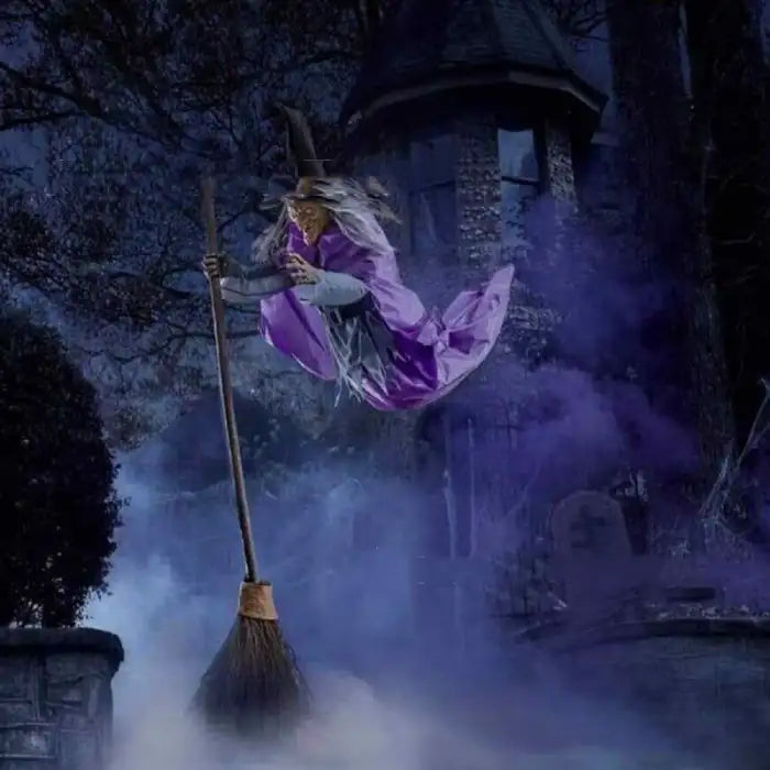 Flying witch yard decor in purple cloak soaring past eerie castle with fog and moonlit background.