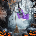 Flying witch yard decor with purple cape hovering above pumpkins on haunted forest path at night.