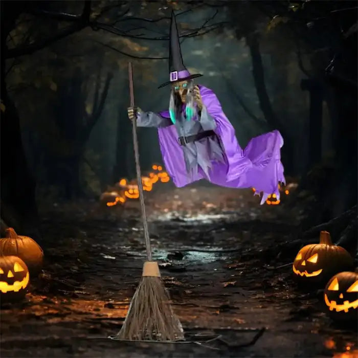 Flying witch yard decor gliding above dirt path lined with glowing pumpkins in shadowy woods.