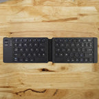 Foldable Bluetooth keyboard fully open on wooden surface, showing keys and power button.