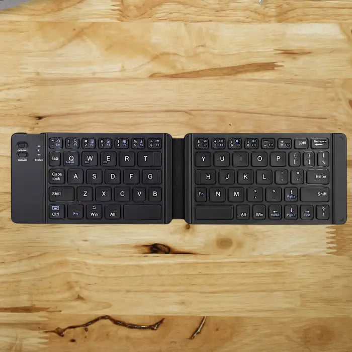 Foldable Bluetooth keyboard fully open on wooden surface, showing keys and power button.