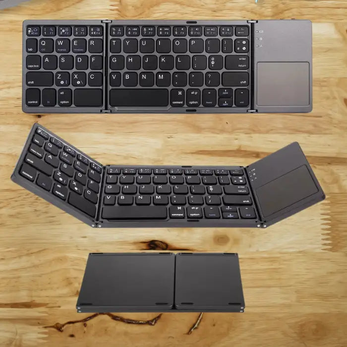 Foldable wireless keyboard with touchpad displayed open and folded on wooden table.