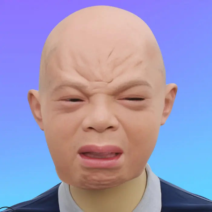 Funny baby mask with sad wrinkled face expression and pinkish eyes worn on adult mannequin head.