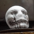 Ghost latex mask placed on surface with black paint dripping from eyes and mouth in creepy effect.