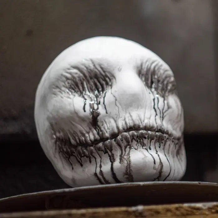 Ghost latex mask placed on surface with black paint dripping from eyes and mouth in creepy effect.