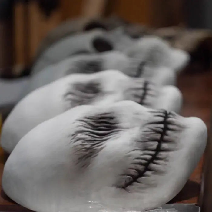 Multiple ghost latex masks lined up on table, showing eerie black eye and mouth detailing.
