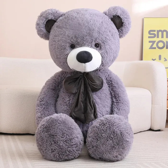 Large brown teddy bear with a bow sitting comfortably on a white sofa.