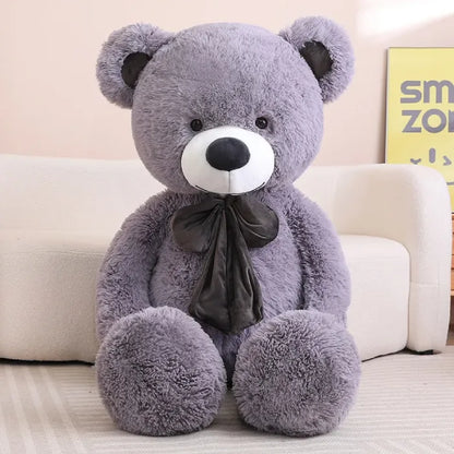 Large brown teddy bear with a bow sitting comfortably on a white sofa.