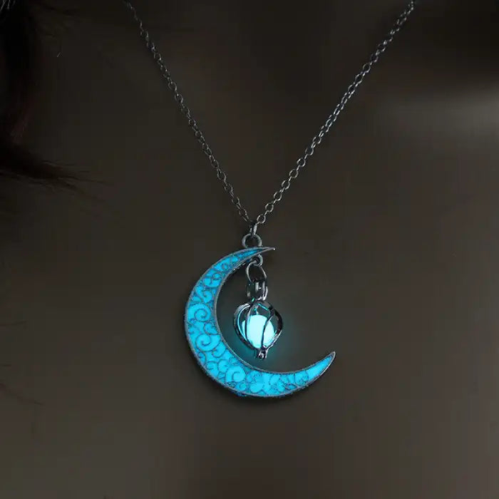 Glowing necklace with blue crescent moon and hanging heart pendant on silver chain, soft glow in dark.