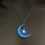 Glowing necklace with crescent moon and bright blue heart charm glowing softly in low light setting.