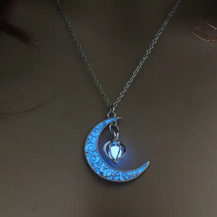 Glowing necklace with crescent moon and bright blue heart charm glowing softly in low light setting.