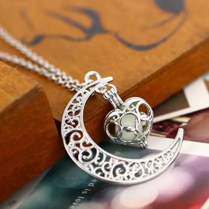 Glowing necklace with silver crescent moon and intricate heart pendant placed on wooden surface.