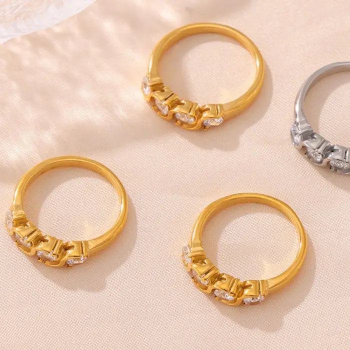 Gold and silver rings with twist designs and cubic zirconia stones displayed on a beige fabric background.