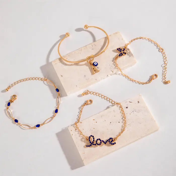 Flat lay of gold bracelets with blue gemstone accents, including floral, heart, and scripted “love” designs.