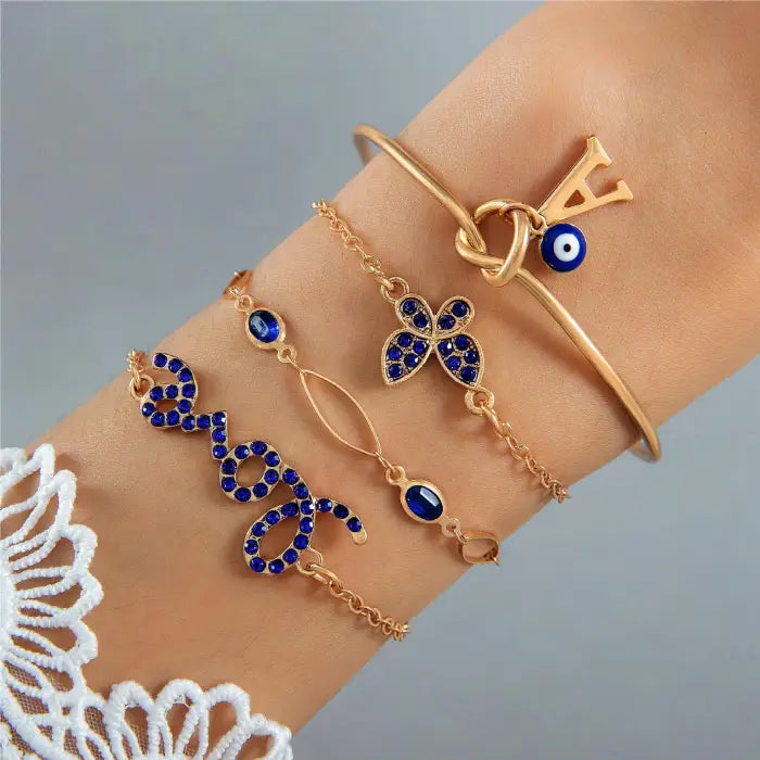 Gold bracelet set with a blue evil eye charm and floral and script “love” designs with blue gemstones.