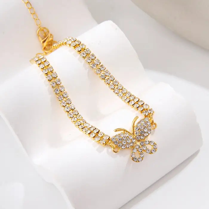 Closeup of a gold butterfly anklet with dazzling crystal details on a white surface for jewelry lovers.