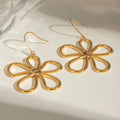 Gold daisy earrings displayed on textured silver plate with dramatic lighting and shadows