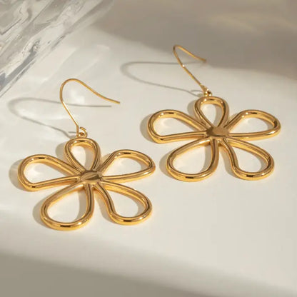 Gold daisy earrings displayed on textured silver plate with dramatic lighting and shadows