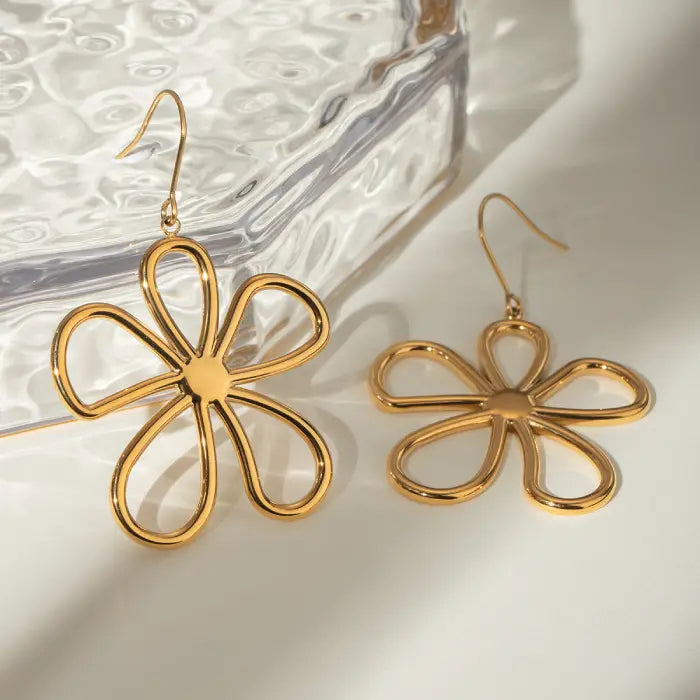 Close-up of gold flower drop earrings showing glossy finish and petal detail against white surface