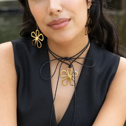 Gold flower pendant on black cord necklace paired with matching earring against black sleeveless top