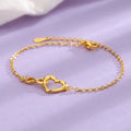 Gold heart infinity bracelet with a sparkling diamond accent, displayed on a soft purple background.