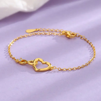 Gold heart infinity bracelet with a sparkling diamond accent, displayed on a soft purple background.