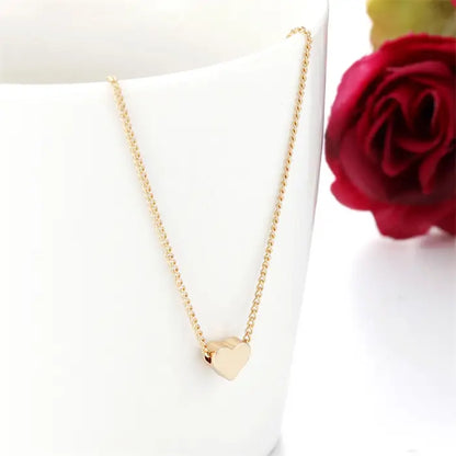 Gold heart pendant necklace displayed with red rose, romantic jewelry styling on white surface