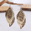 A pair of gold-toned layered earrings with leopard print and glitter details displayed on a wooden surface.