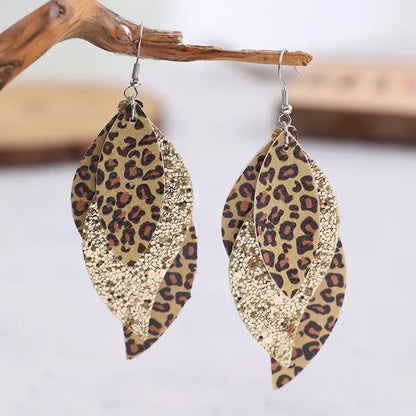 A pair of gold-toned layered earrings with leopard print and glitter details displayed on a wooden surface.