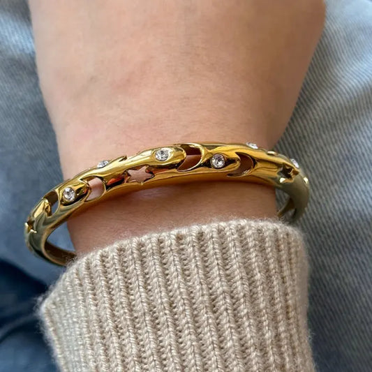 Stylish gold plated bangle with celestial moon and star cutouts, worn on wrist with cozy sweater for a chic look.