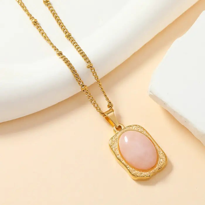 Gold rectangular pendant with pink stone and textured frame, perfect for elegant jewelry lovers.