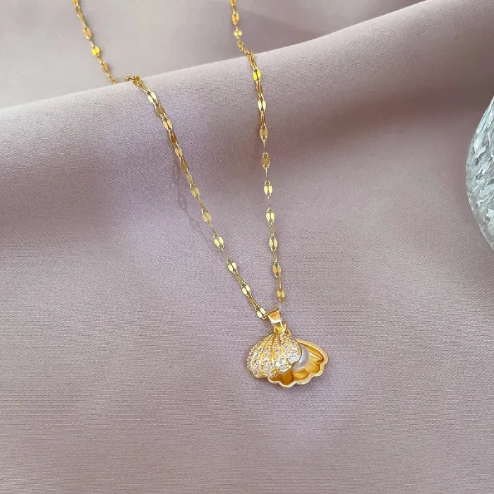 gold seashell necklace featuring open shell pendant revealing pearl inside on soft fabric background