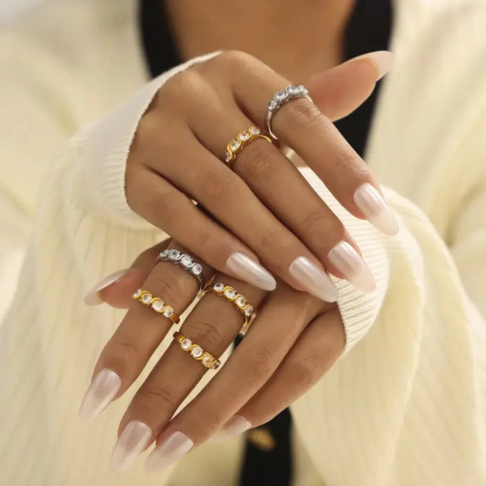 Close-up of hands wearing stacked gold and silver rings with cubic zirconia stones, styled with neutral nails.