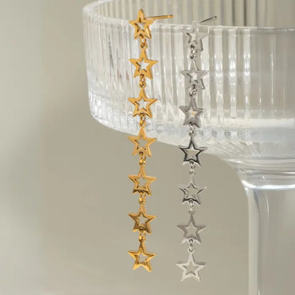 Contrasting gold and silver star drop earrings hanging on crystal glassware