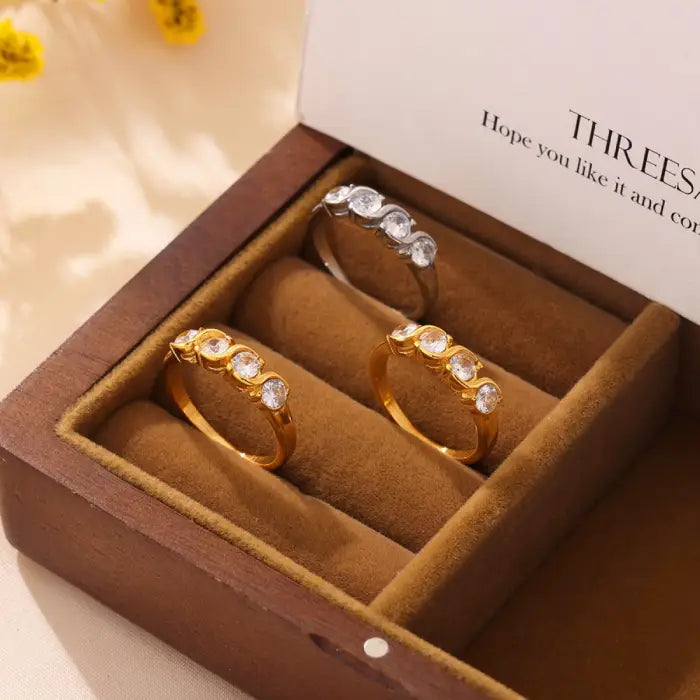 Gold and silver cubic zirconia rings displayed in a velvet-lined gift box with a wooden frame.