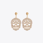 Gold skull-shaped dangle earrings adorned with clear rhinestones on a white background.