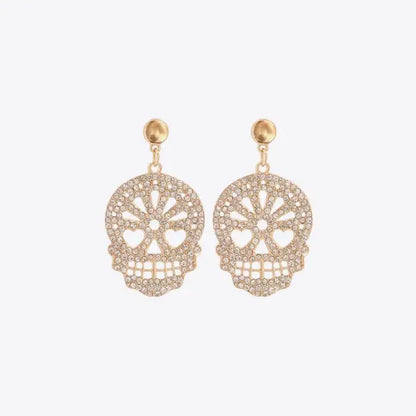 Gold skull-shaped dangle earrings adorned with clear rhinestones on a white background.