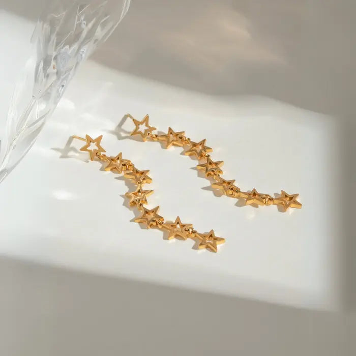 Gold linked star earrings arranged in curved pattern on white surface