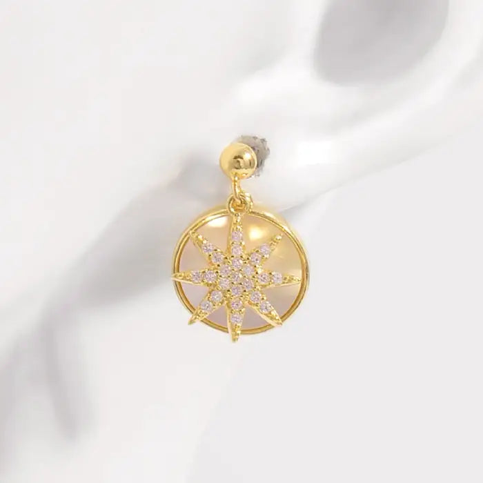 Close-up of single gold starburst earring with crystal embellishments on circular mother of pearl backdrop